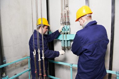 Machinists adjusting lift in elevator hoistway clipart