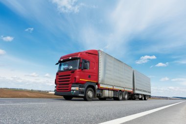 Red lorry with grey trailer over blue sky clipart