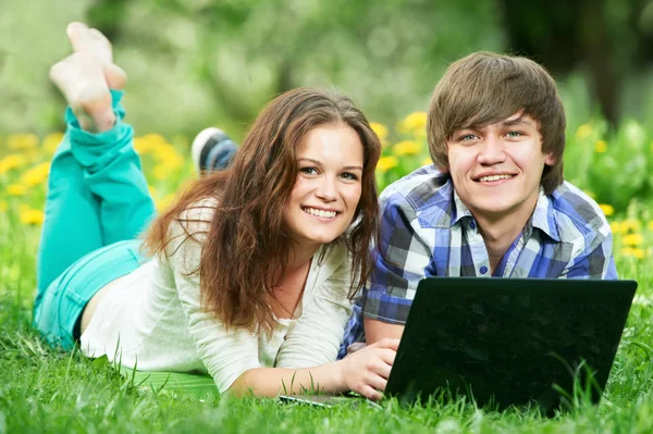 Два улыбающихся молодых студента с компьютером на улице — стоковое фото
