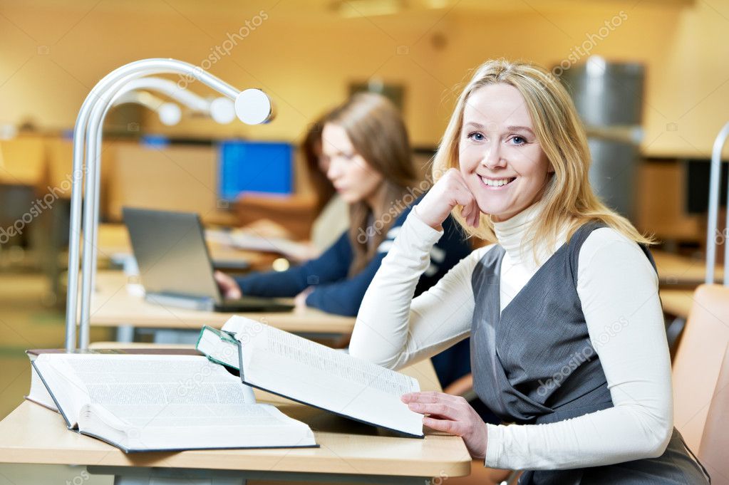 Smiling young adult woman reading book in library