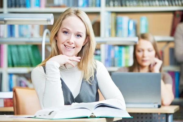 Smiling young adult woman reading book in library — Stock Photo, Image