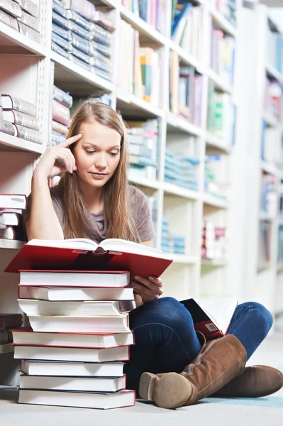 Усміхнена молода доросла жінка читає книгу в бібліотеці — стокове фото