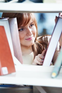 Young student girl at book shelf in library clipart