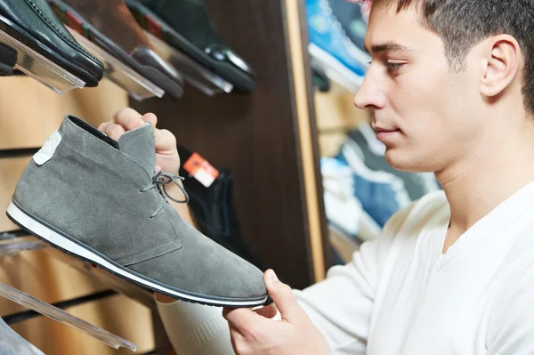 Jeune homme choisissant chaussure dans le magasin de vêtements — Photo