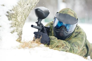 Paintball player with marker at winter outdoors clipart