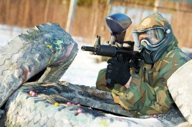 Paintball player with marker at winter outdoors clipart