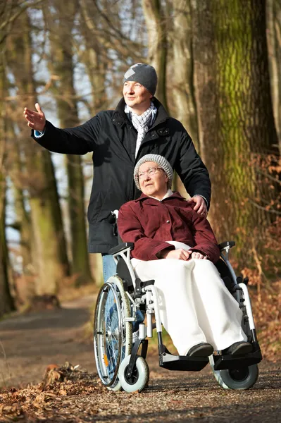 Elderly woman in wheelchair walking with son — Stockfoto