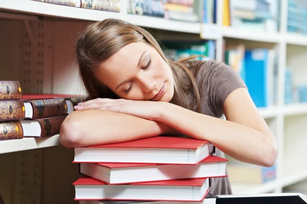 Tired young woman sleeping on book in library — Stock Photo, Image