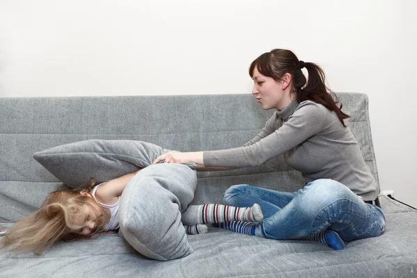 Bambino piccolo e giovane madre cuscino lotta sul divano . — Foto Stock