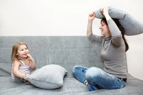 Little child and young mother pillow fighting on the sofa. — Stock Photo, Image