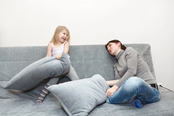 Little child and young mother pillow fighting on the sofa. — Stock Photo, Image