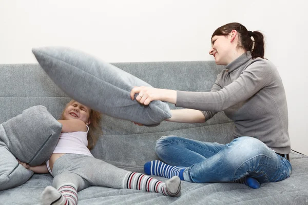 Little child and young mother pillow fighting on the sofa. — Stock Photo, Image