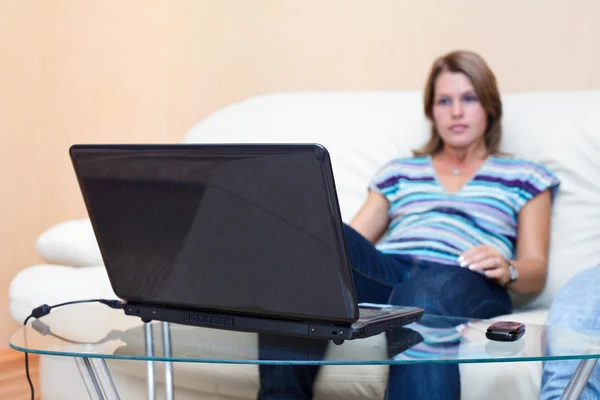 Одна красива жінка сидить на дивані і дивиться на екран ноутбука. Жінка це — стокове фото
