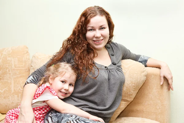 Mãe e sua filhinha sentados e sofá e abraços — Fotografia de Stock