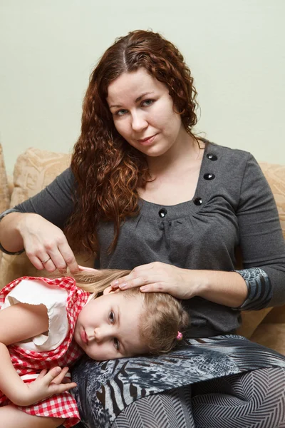 Mother and little daughter sitting on couch. Woman combing daughter hair — Stock Photo, Image