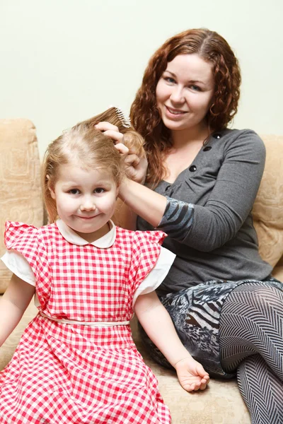 Μητέρα και κορούλα που κάθεται στον καναπέ. γυναίκα κτενίσματος κόρη μαλλιά — Φωτογραφία Αρχείου