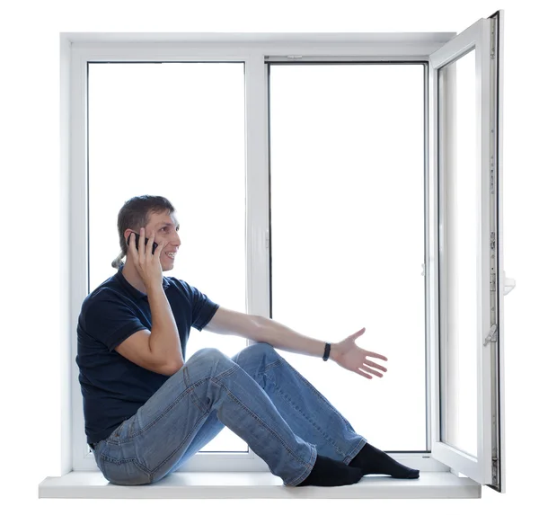 Handsome man sitting on windowsill and calling on phone — Stock Photo, Image