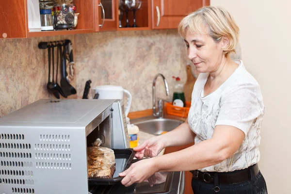 Mogen kvinna som står i köket nära öppnade spis — Stockfoto