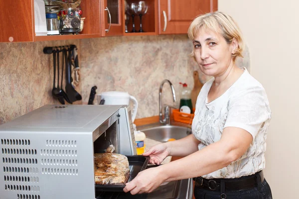 Mature woman standing in kitchen near opened stove — Stock Photo, Image