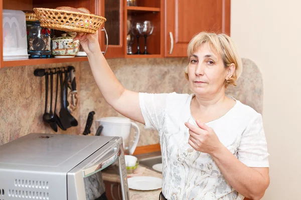 Reife Frau steht in Küche mit Brotkorb — Stockfoto