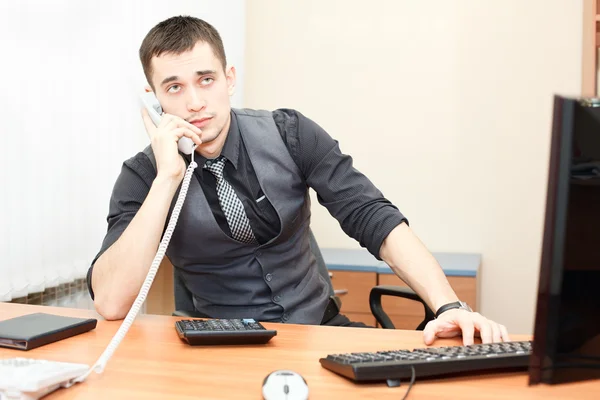 Uomo d'affari intelligente che parla al telefono mentre lavora sul computer desktop — Foto Stock