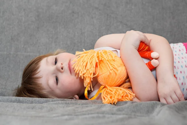 Klein meisje slaapt met doll speelgoed op Bank. — Stockfoto