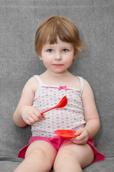 Ritratto di bambina che gioca sul divano con cucchiaio e giocattoli del piatto — Foto Stock