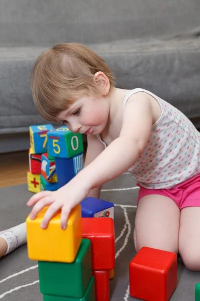 Porträtt av liten flicka som leker med tegel på golvet — Stockfoto
