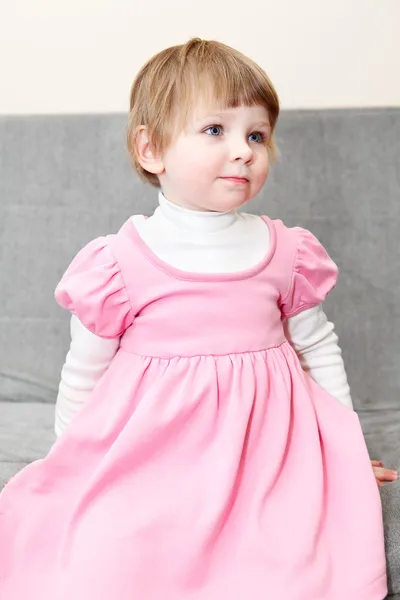 Porträtt av liten flicka i rosa klänning sitter på soffan och tittar — Stockfoto