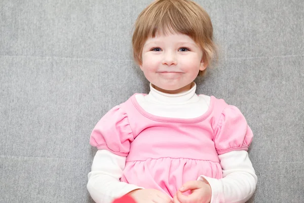 Portret van klein meisje in roze jurk zittend op een bank en op zoek — Stockfoto