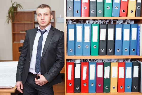 Yakışıklı erkek business executive ayakta arkasında bir kitaplık — Stok fotoğraf
