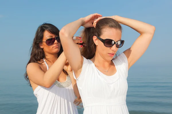 Молодая женщина одевает волосы своего друга на берегу моря — стоковое фото