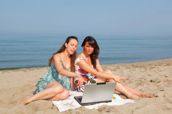 Две женщины с компьютером на берегу моря — стоковое фото