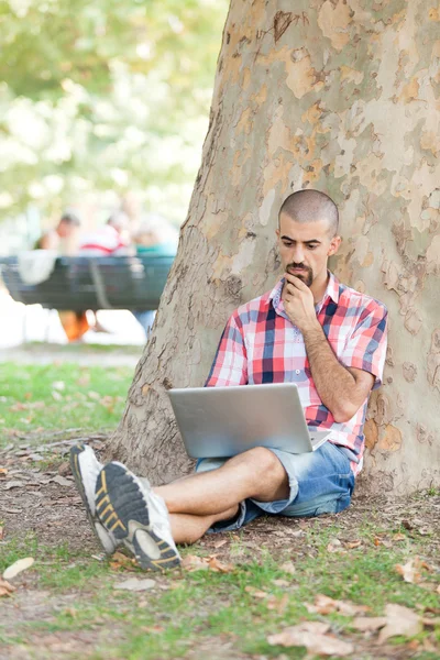 Jongeman met computer in park — Stockfoto