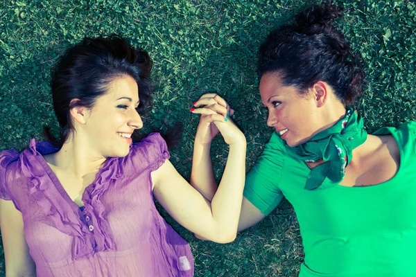 Две девушки лежат на траве и держатся за руки — стоковое фото