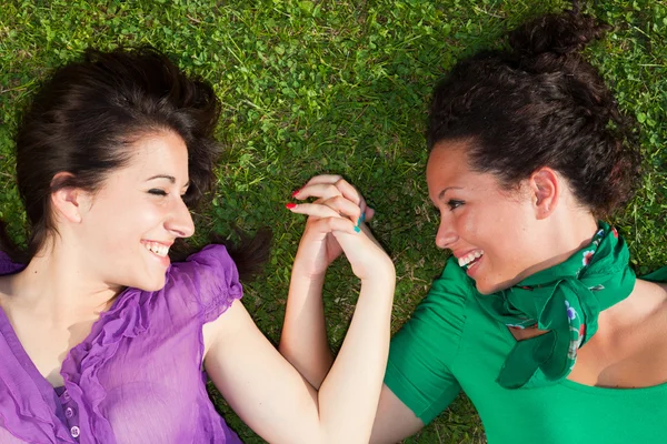Dwie dziewczyny, leżąc na trawie i trzymając się za ręce — Zdjęcie stockowe