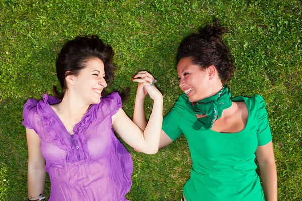 Две девушки лежат на траве и держатся за руки — стоковое фото