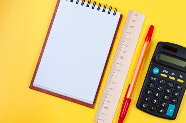 Cuaderno de bolsillo y calculadora sobre fondo amarillo . — Foto de Stock
