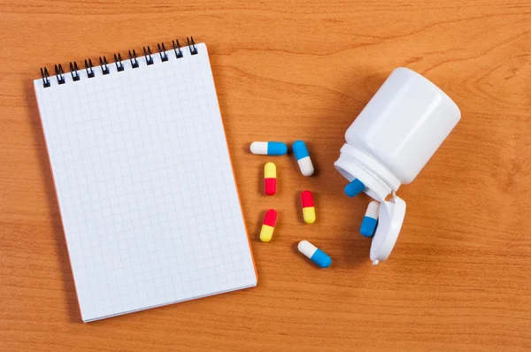 stock image Notebpad and pills on table top view.