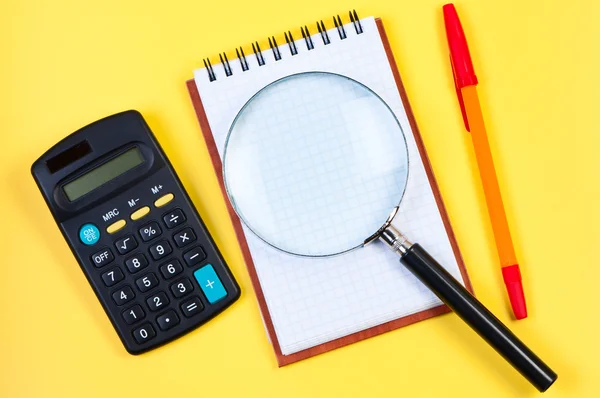 Электронный калькулятор, блокнот и лупа на желтом . — стоковое фото