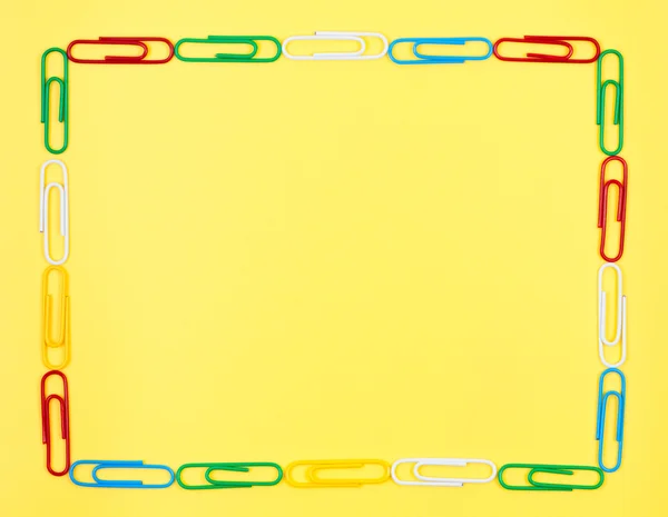 stock image Frame of colorful paper clips on yellow background.