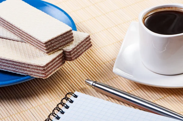 Tasse Kaffee mit Waffeln. Notizblock und Stift auf dem Tisch. — Stockfoto