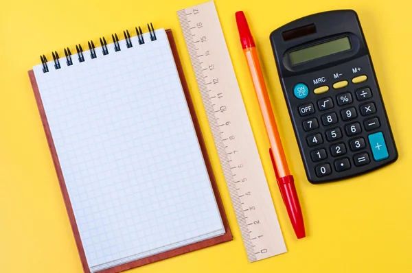 Miniräknare och anteckningar på gul bakgrund ovanifrån. — Stockfoto