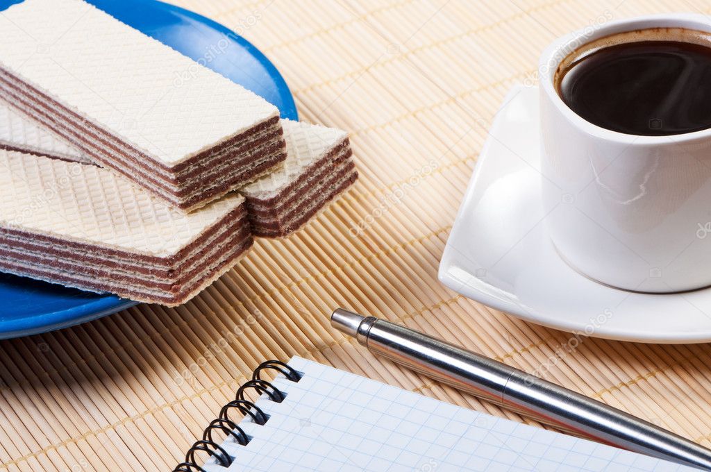 Cup coffee with waffles. Notepad and pen on table.