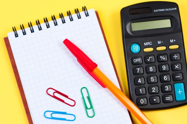 Kladblok met pen en papier clips, rekenmachine in de buurt van. — Stockfoto