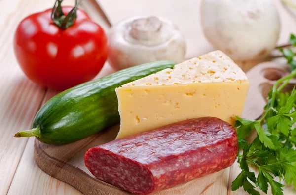Korv och ost med grönsaker på skärbräda. — Stockfoto