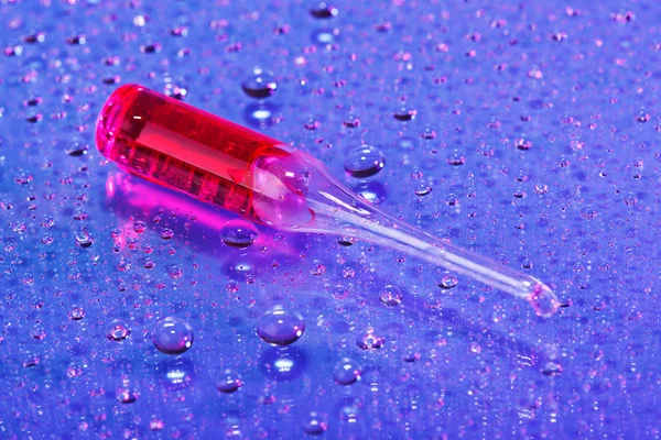 Ampolla roja sobre fondo abstracto de gotas de agua, vista macro — Foto de Stock