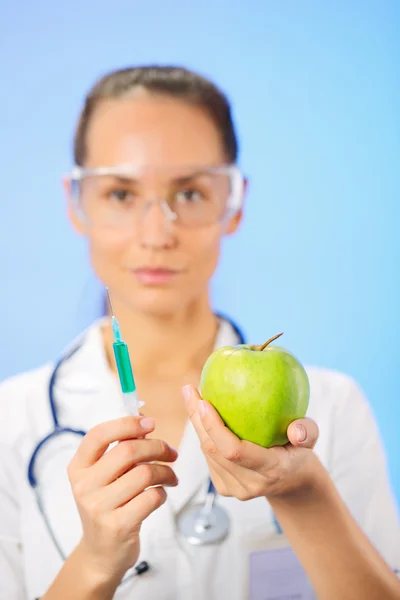 Junge Ärztin spritzt grünen Apfel mit Spritze auf blau — Stockfoto