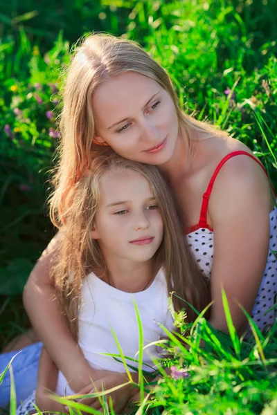 漂亮的妈妈和女儿坐在郁郁葱葱的绿草草甸上 — 图库照片