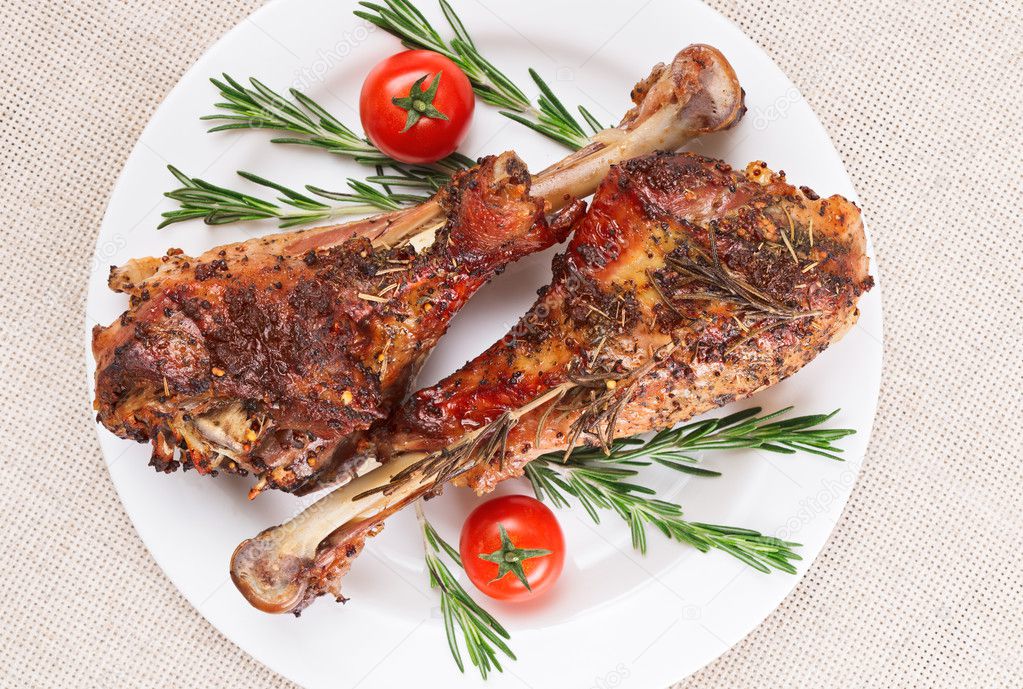 Roasted turkey legs on white plate with cherry tomato and rosema